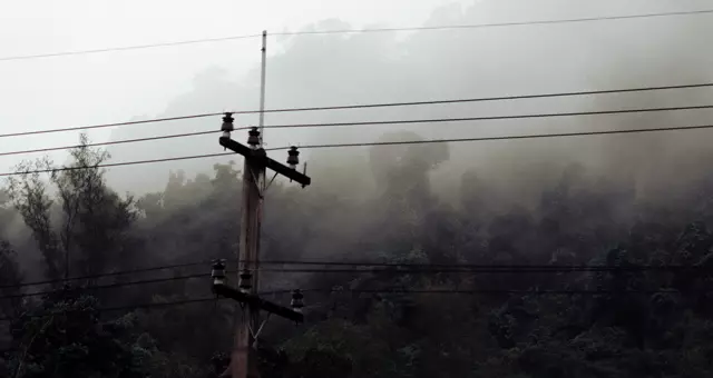 A picture of a powerline in the hills with fog